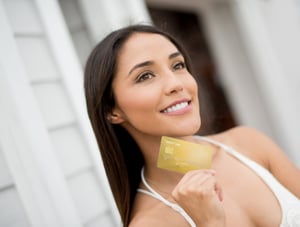 A smiling woman holding up a credit card with her right hand.